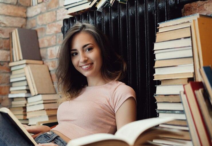 Young woman reading book surrounded by stacks of books in cozy library with brick walls