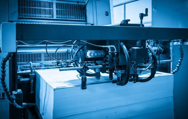 Industrial paper cutting machine slicing large stack of paper in printing or book manufacturing facility