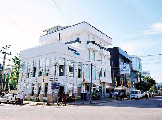 Modern white multi-story building with Minarai garden sign and Sri Lankan flags on a sunny street